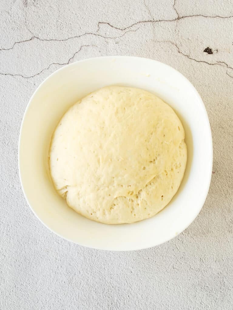 White bowl with risen donut yeast dough. Cement background, top view.