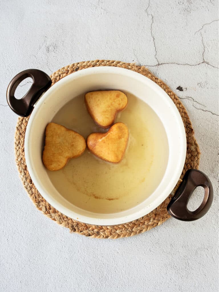 White and black saucepan with oil and fried heart-shaped doughnuts. Gray background, top view.