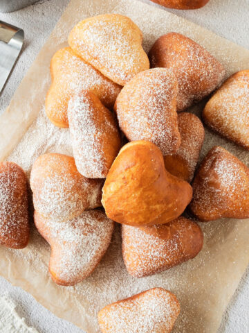 Parchment paper with pile of heart donuts. Top view. White background.