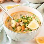 Light gray bowl of turkey soup with vegetables. Lemon wedge, spoon. Light-colored background.