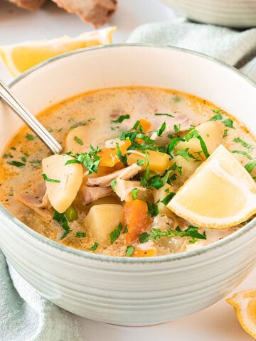 Light gray bowl of turkey soup with vegetables. Lemon wedge, spoon. Light-colored background.