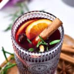 Close up glass with mulled spiced wine with cinnamon stick and orange slices. Wooden and white background.