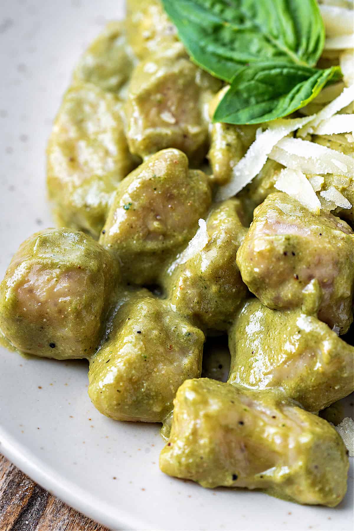 Close up mound of gnocchi with creamy pesto. Whitish plate, basil leaves.