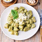 Creamy basil pesto gnocchi on a white plate. Wooden surface.