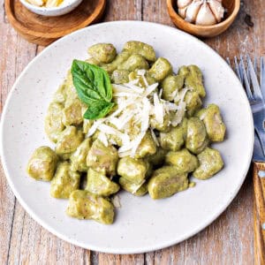 Creamy basil pesto gnocchi on a white plate. Wooden surface.