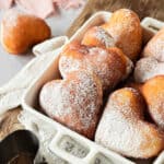 A white baking dish with heart-shaped doughnuts. Pink towel, gray background.