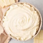 Top view of limestone bowl with white chocolate buttercream. Beige gray background.
