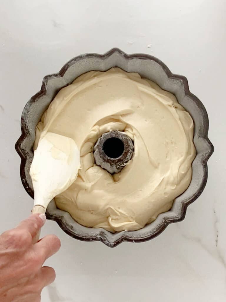 Smoothing cake batter in a dark bundt pan with a white spatula. Top view, white background.