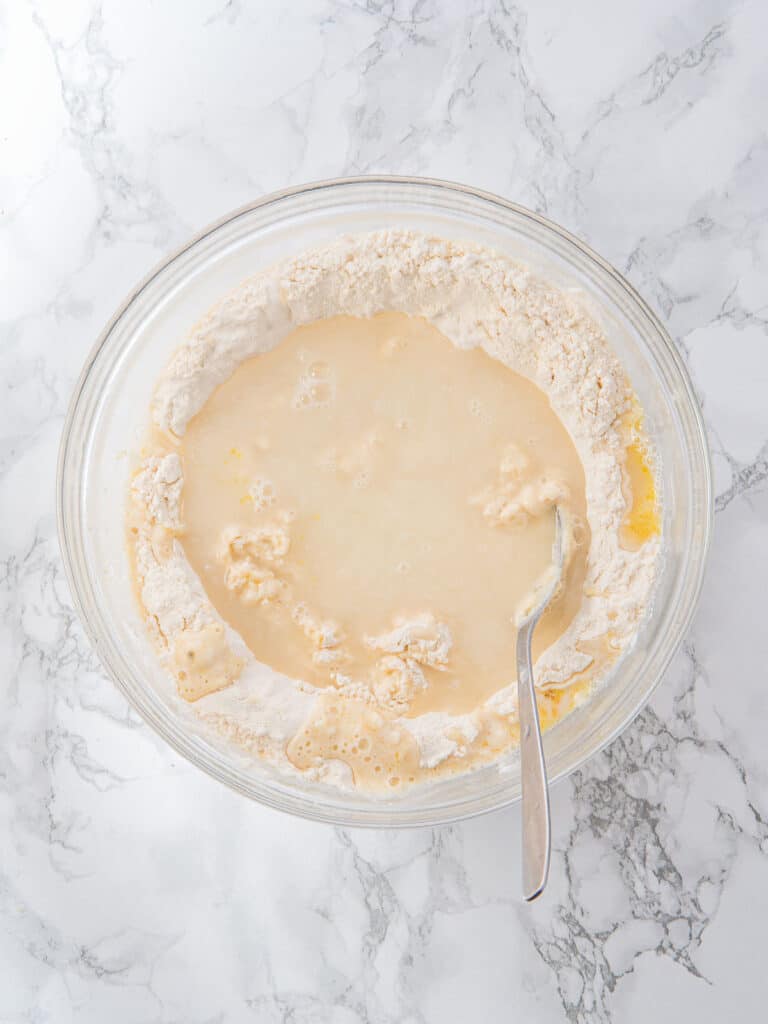Glass bowl with liquids and flour mixture for focaccia dough. Marbled background. Top view. 