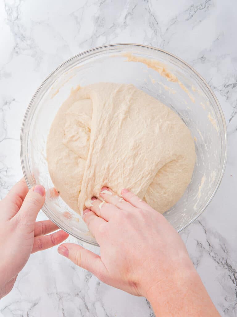 Folding focaccia dough onto itself in a glass bowl. Top view. Marbled background.