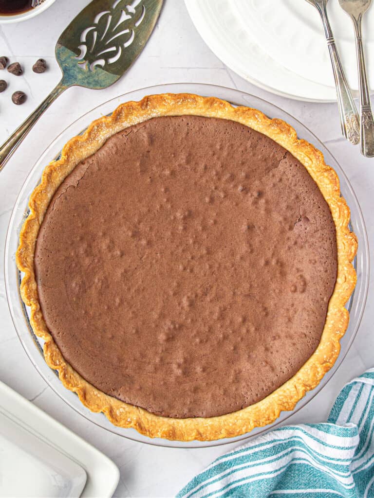 Baked chocolate chess pie on a white surface. Top view. Metal server, teal striped cloth.