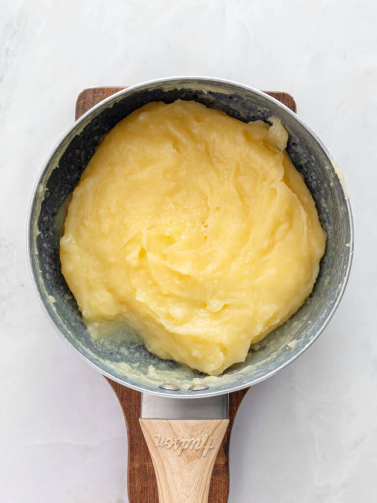 Gray saucepan with pastry cream on a wooden board. Light gray background.