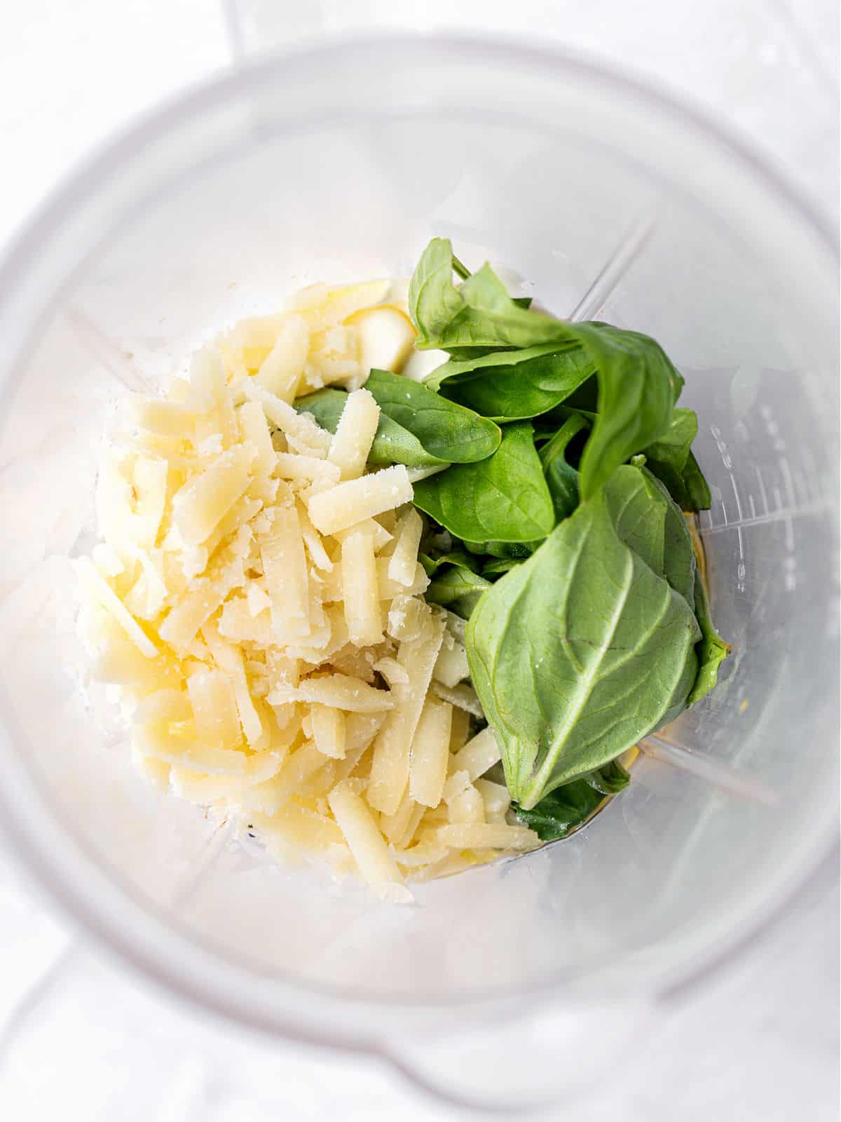 Basil leaves, grated cheese and other ingredients for pesto in the blender jar.