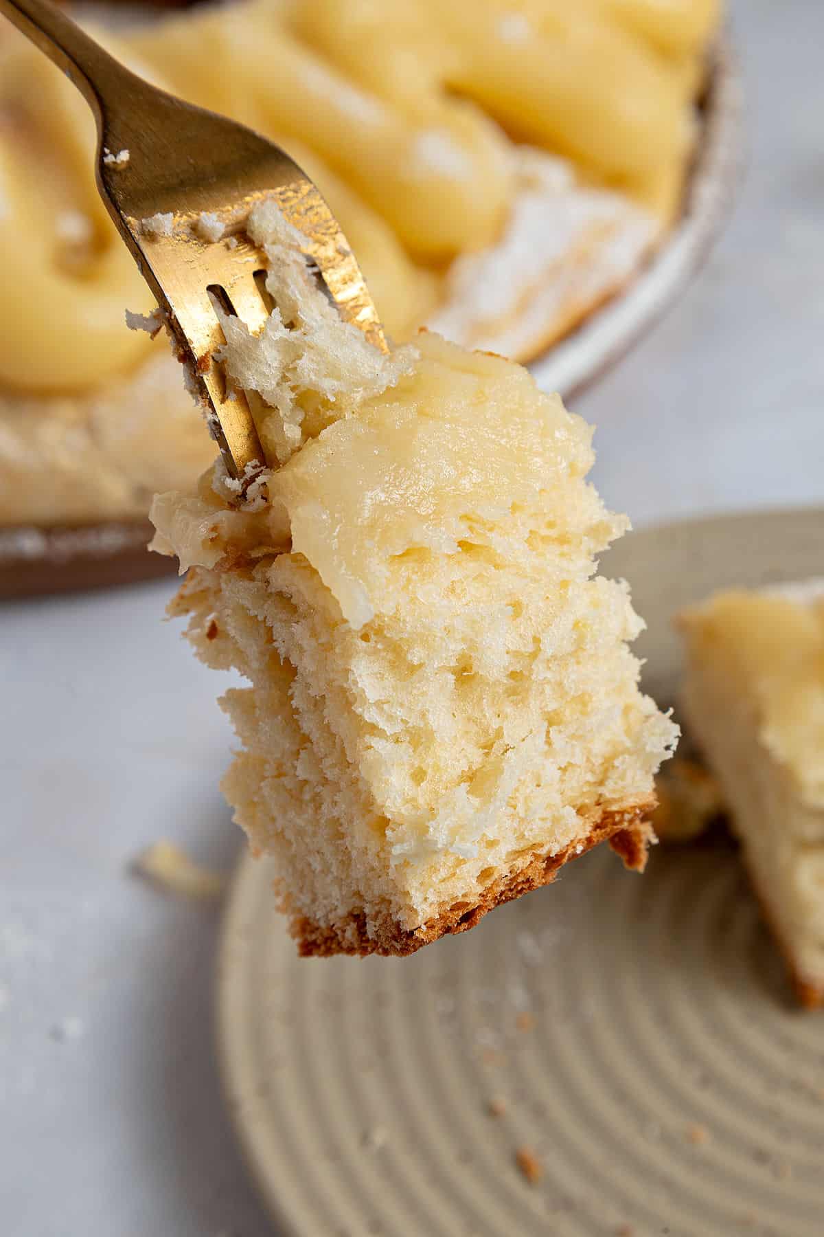 Close up fork with bite of Easter bread over beige plate and more bread on a gray surface.