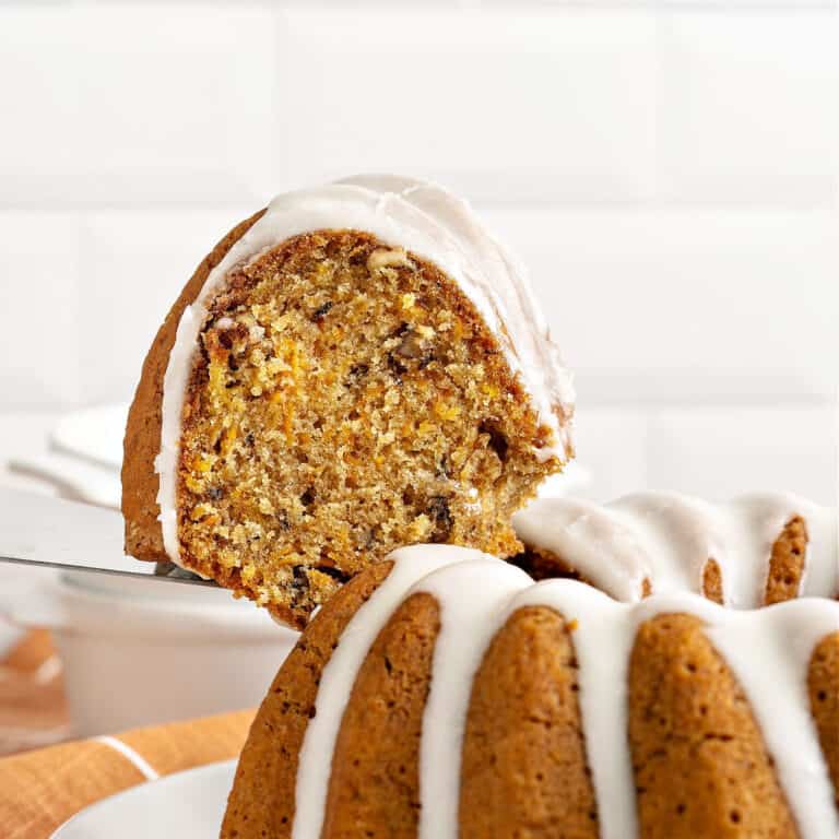 Glazed carrot bundt cake slice being lifted from whole cake. White background.