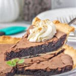 Close up slice of chocolate chess pie with cream dollop being lifted over whole pie.