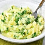 Colcannon mashed potatoes with kale in a light gray plate. A silver wooden fork.
