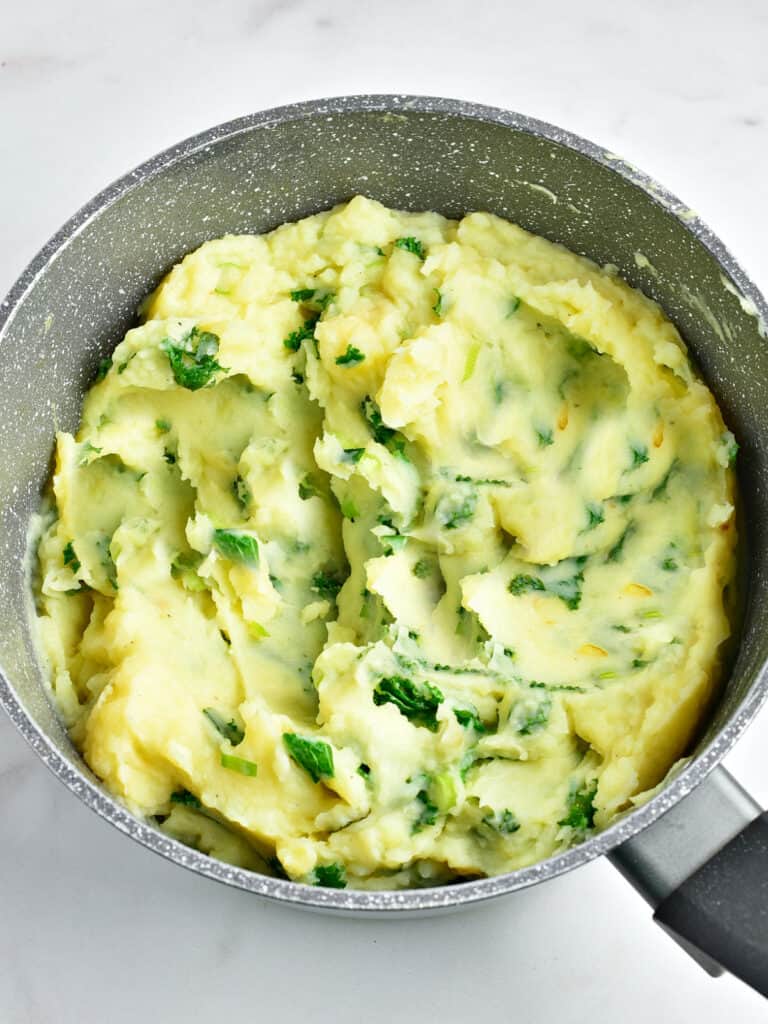 Gray saucepan with mashed potatoes and kale. Top view. Light gray background.