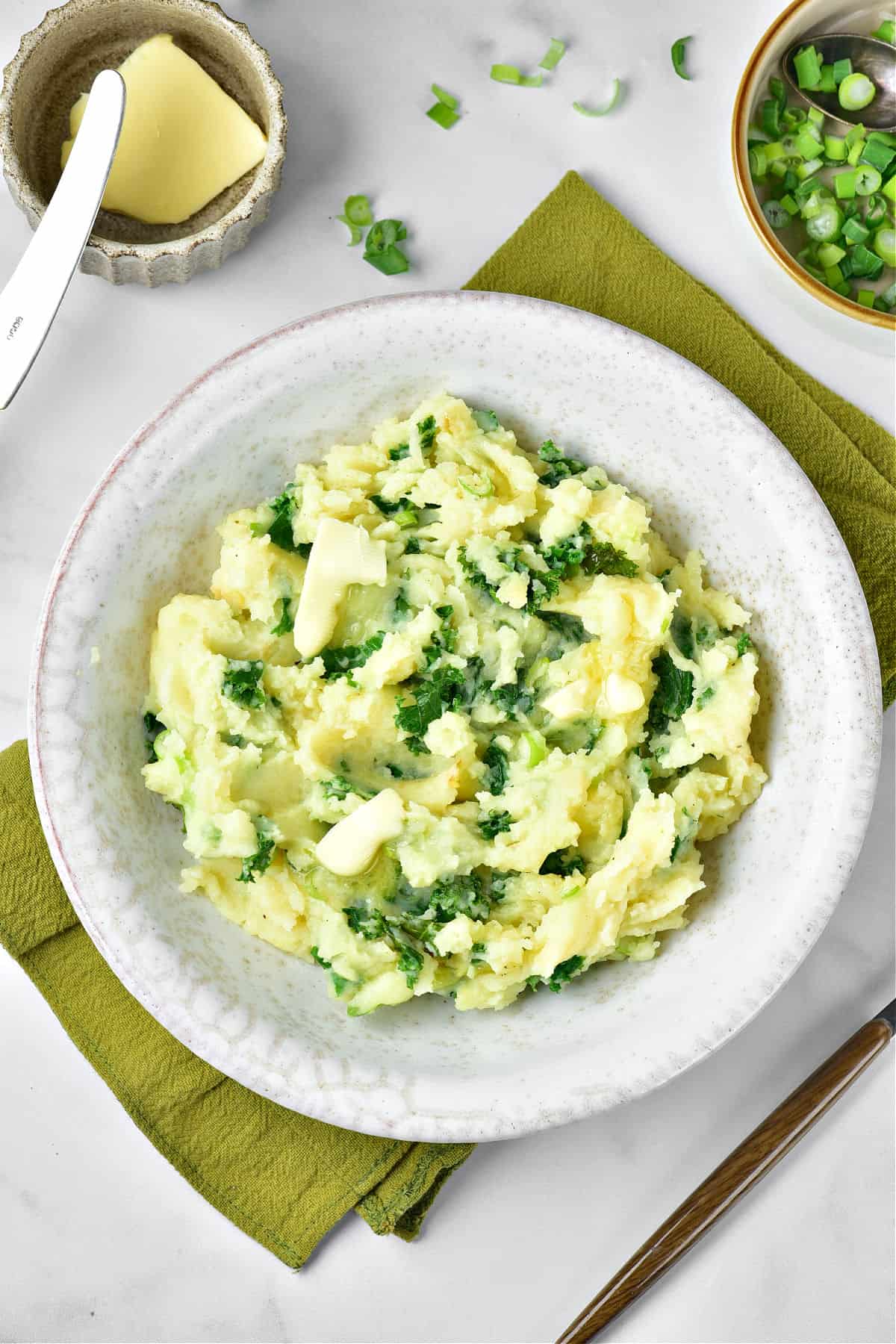 Light gray plate of mash with kale on a olive towel. Light gray background. Top view. Bowl with butter.