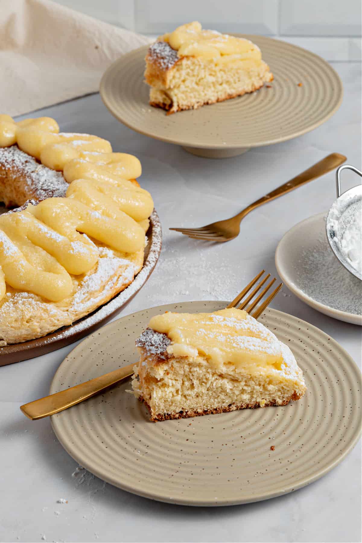 Beige plates with pastry cream topped Easter bread slices. Gray background, gold forks.