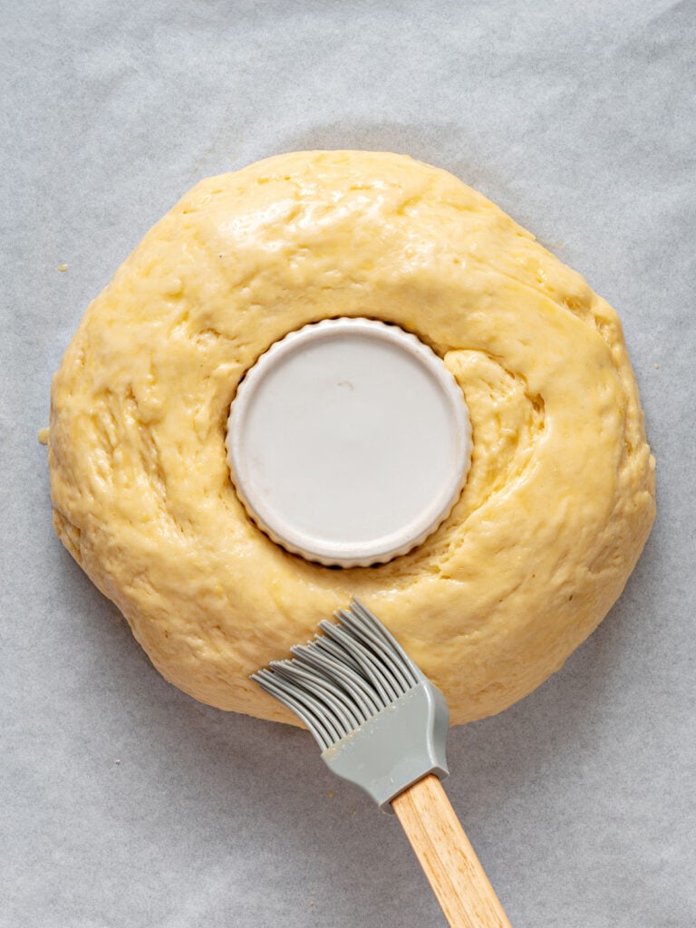 Brushing a risen dough ring with egg wash. Gray pastry brush and background.