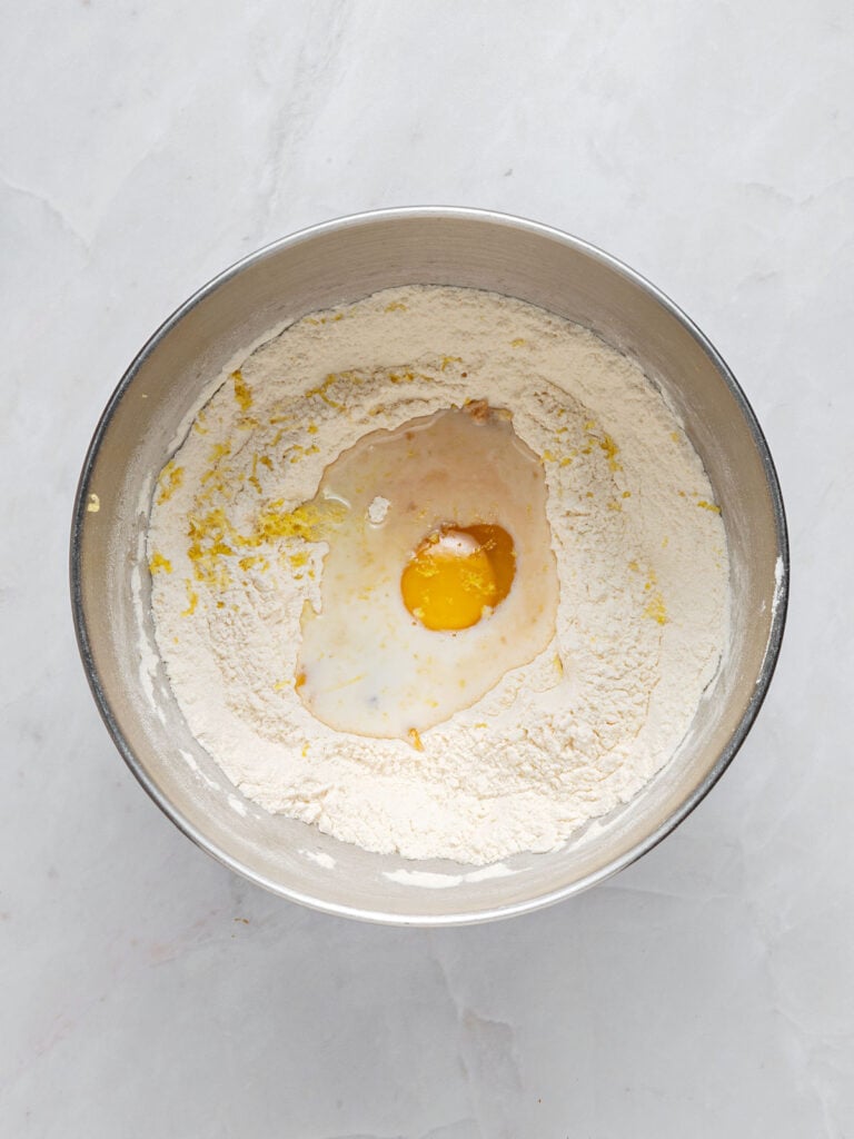 Egg and milk added to flour mixture in a metal bowl. Light gray background. Top view.