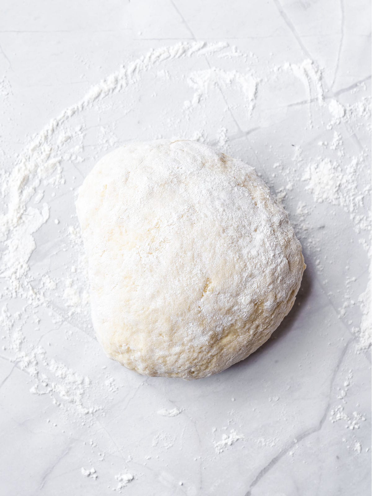 Floured ball of gnocchi dough on a lightly floured marbled surface.