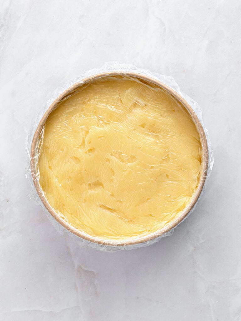 Plastic-covered bowl with pastry cream. Light gray background.