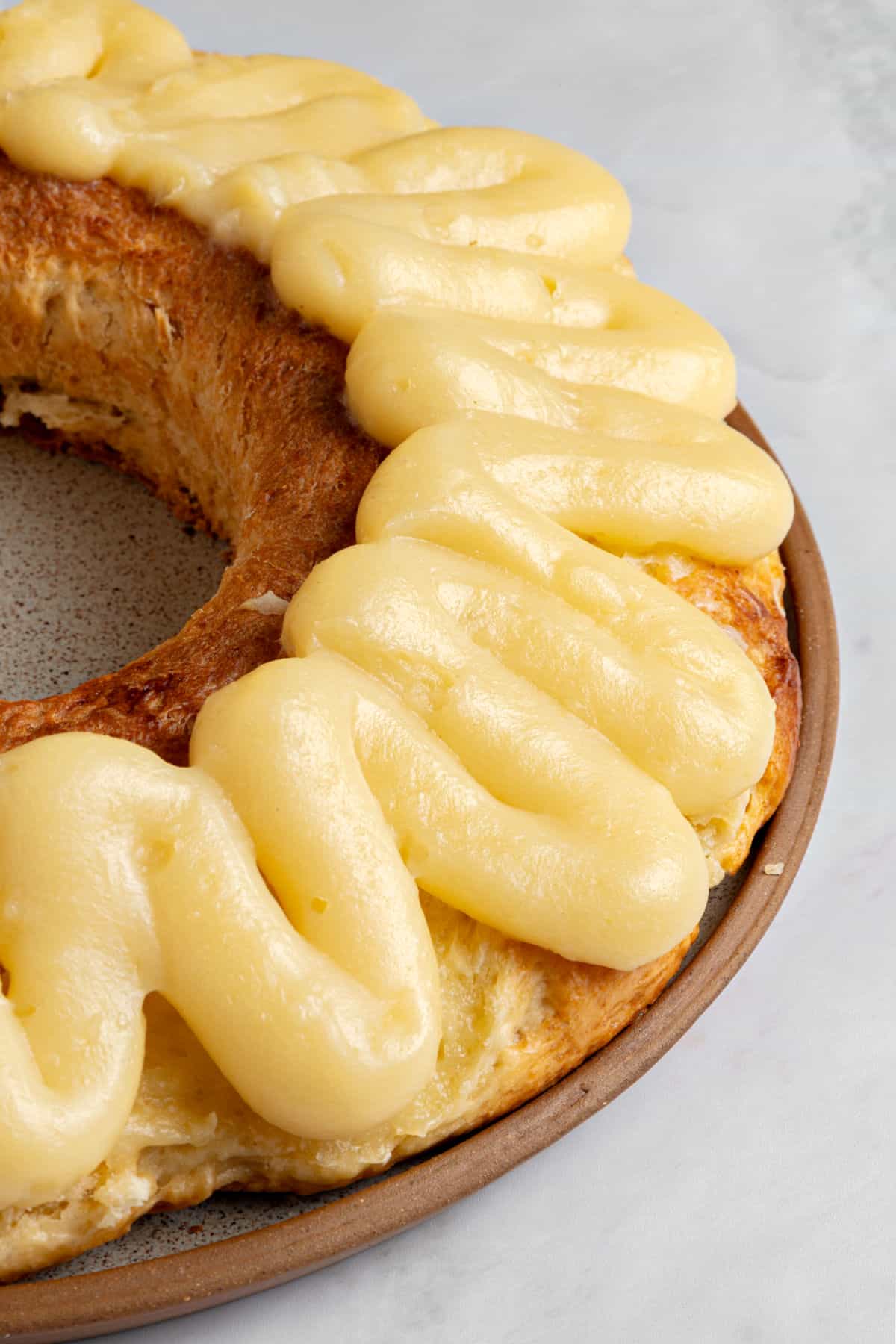 Partial view of bread ring topped with pastry cream. Light gray background.