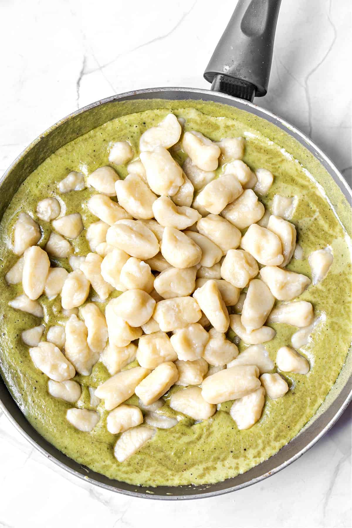 Cooked gnocchi on a creamy pesto sauce in a skillet. White background.