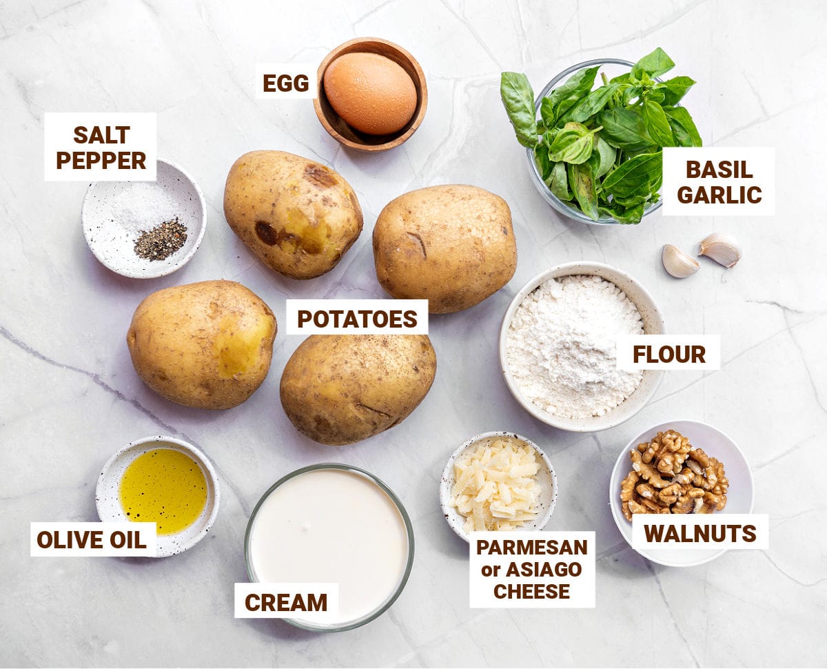 Ingredients for potato gnocchi and basil walnut pesto in bowls on a white background.
