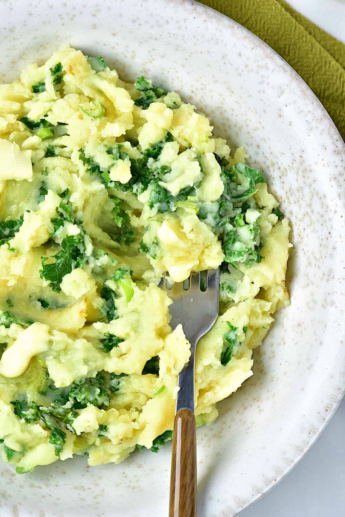 Partial gray plate with colcannon with kale. Silver wooden fork.
