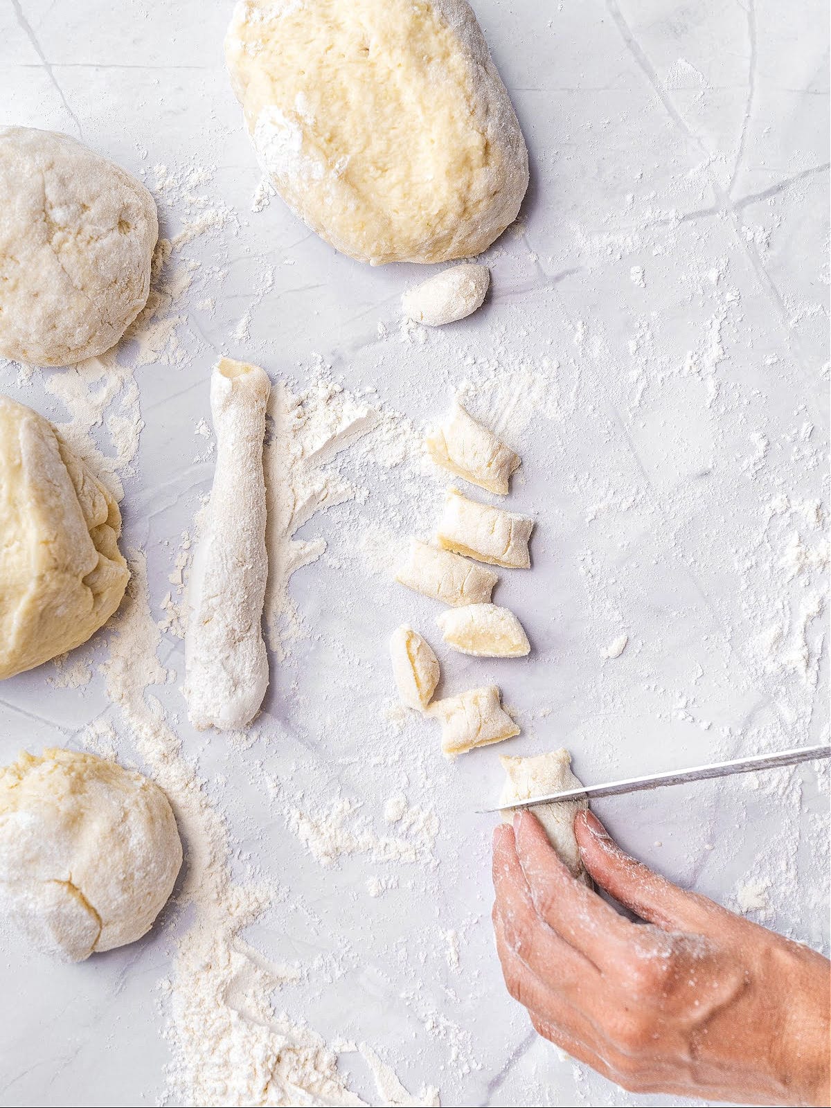 Cutting gnocchi pieces on a floured light gray surface. Top view.