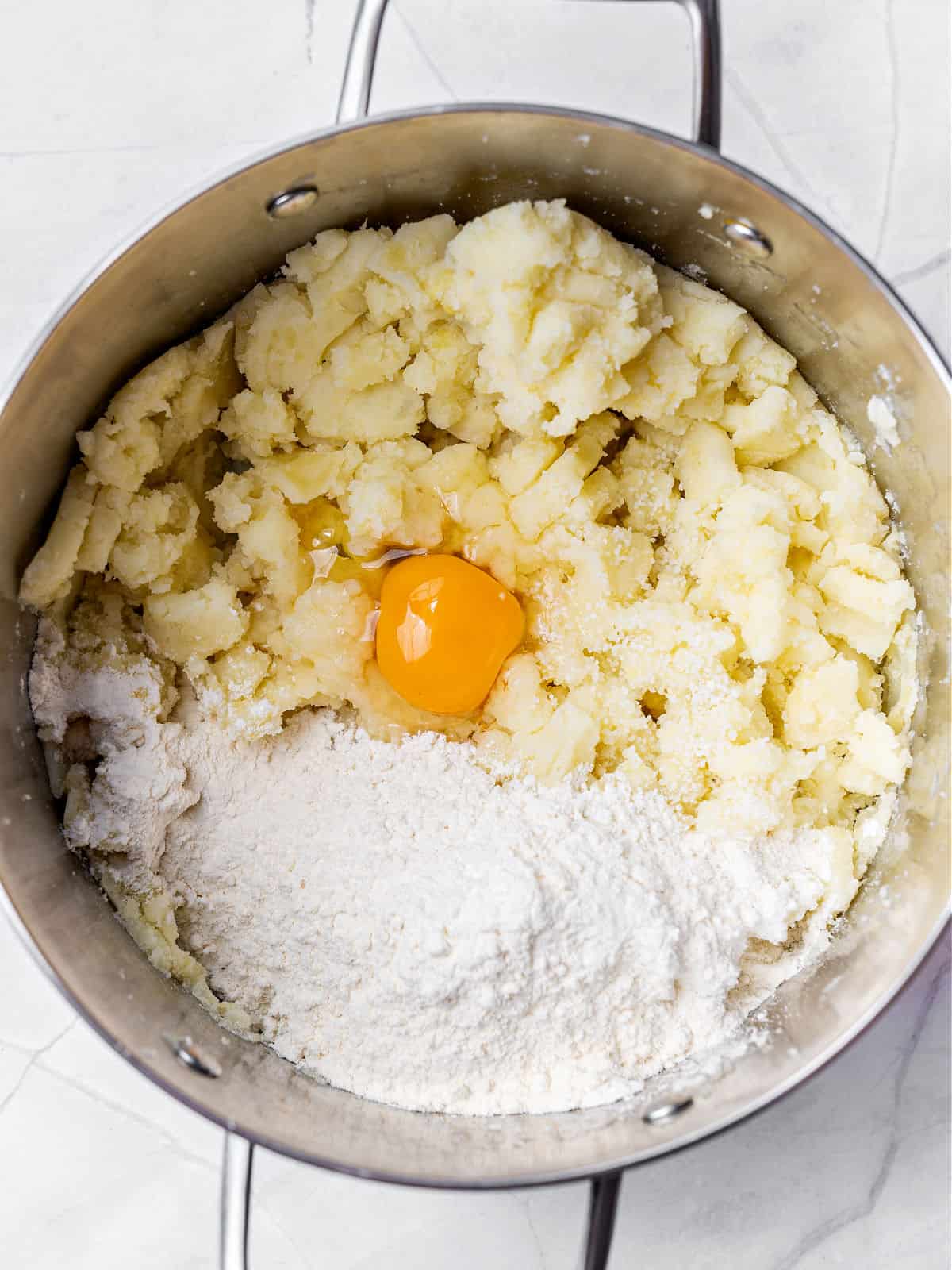 Large metal pot with mashed potatoes, egg and flour.