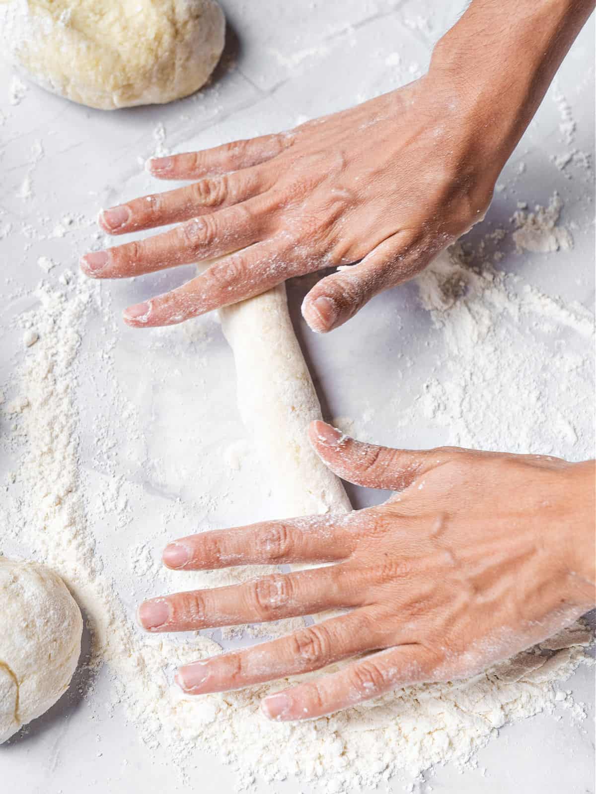 Hands rolling ropes of gnocchi dough. Light gray floured surface.