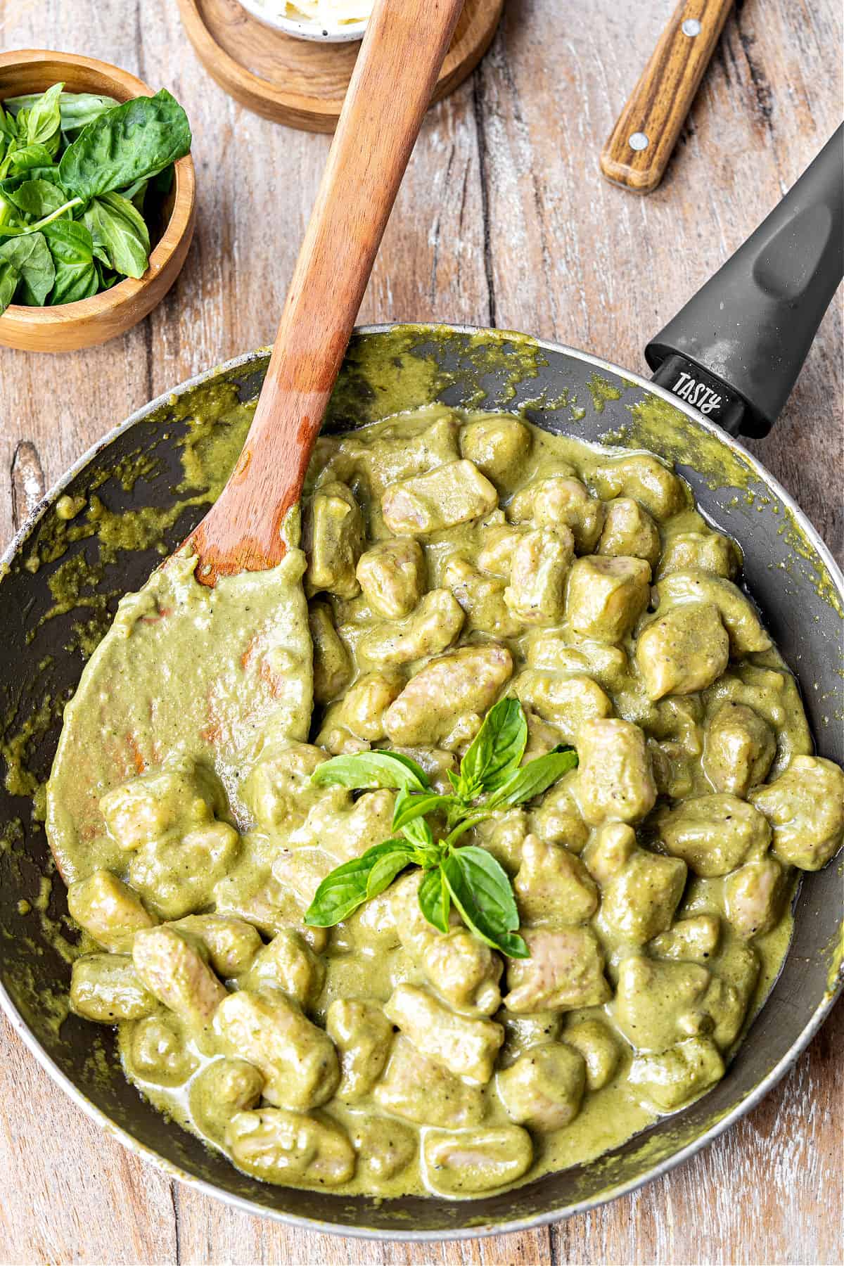 Skillet with basil pesto gnocchi. Wooden spoon and surface.