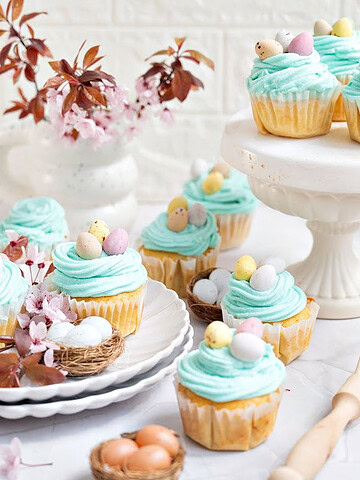 Aqua colored Easter cupcakes in white plates and cake stand. Mini eggs, white background.