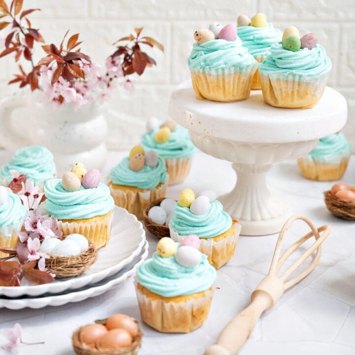 Aqua colored Easter cupcakes in white plates and cake stand. Mini eggs, white background.
