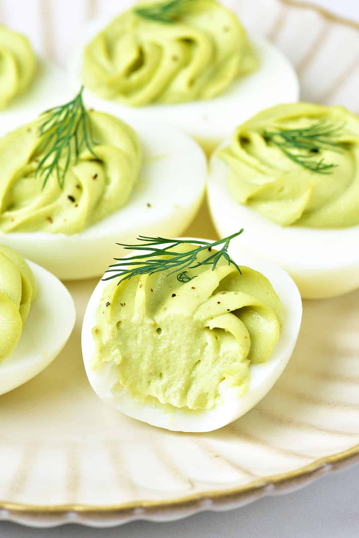 Bitten avocado deviled egg with more filled eggs on a white plate.