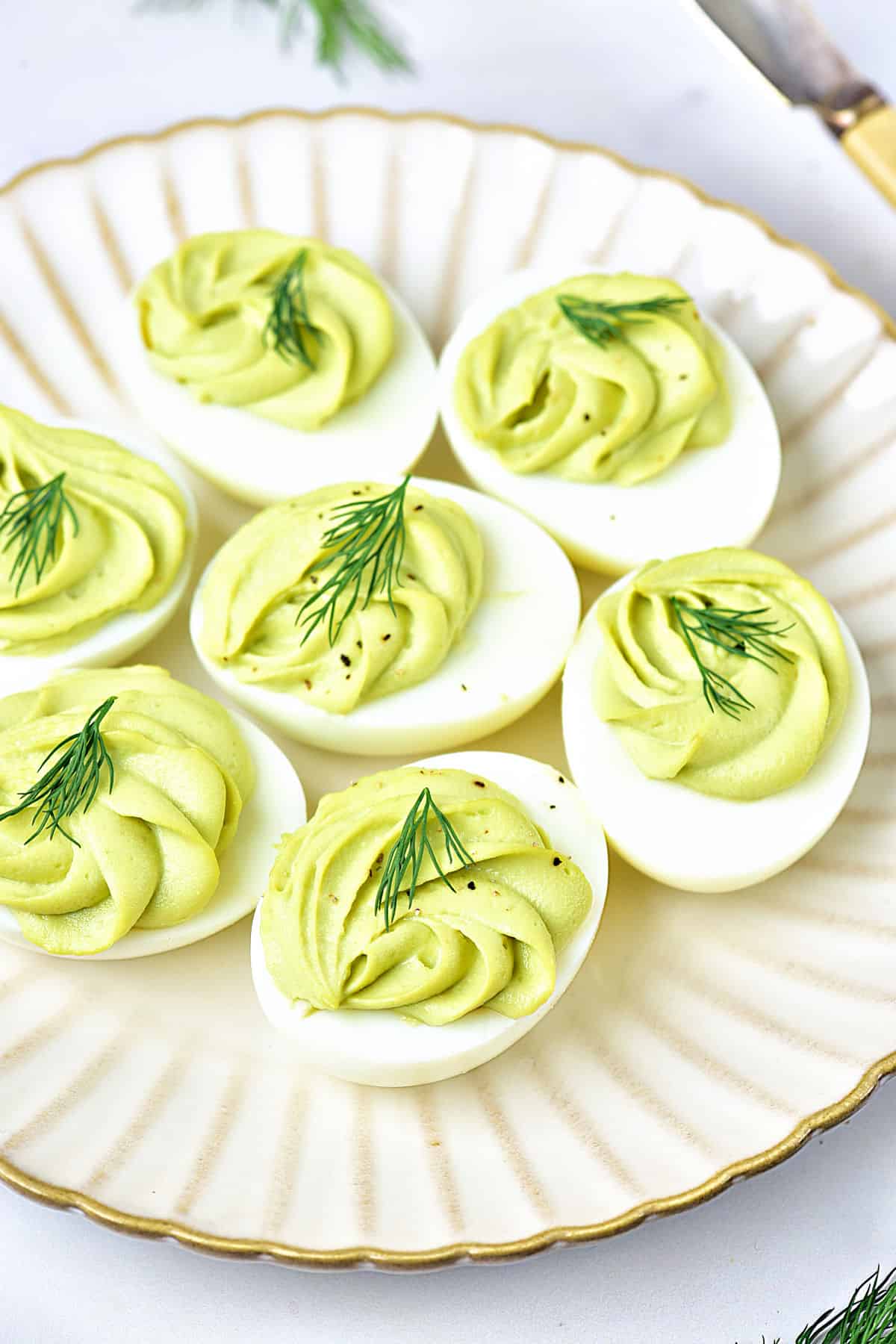 White plate with avocado deviled eggs and dill sprigs.