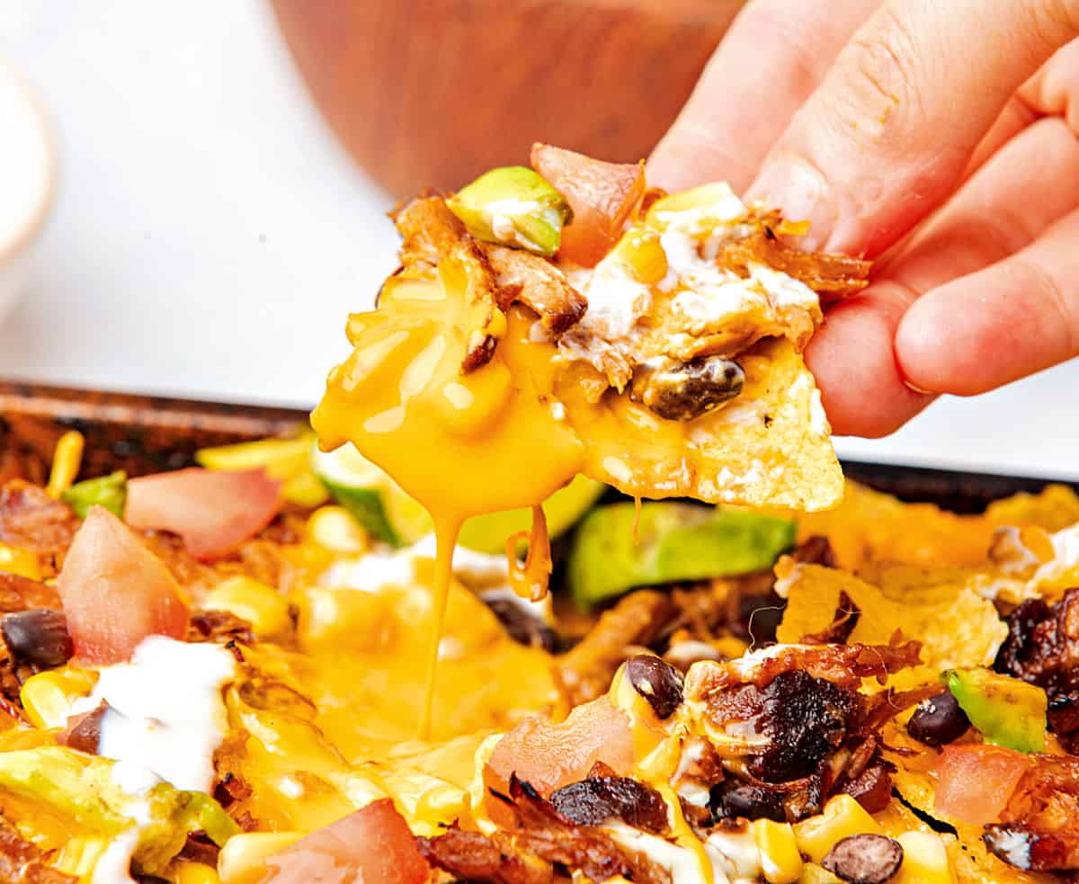 Lifting a cheesy nacho with pork and beans from bake tray.