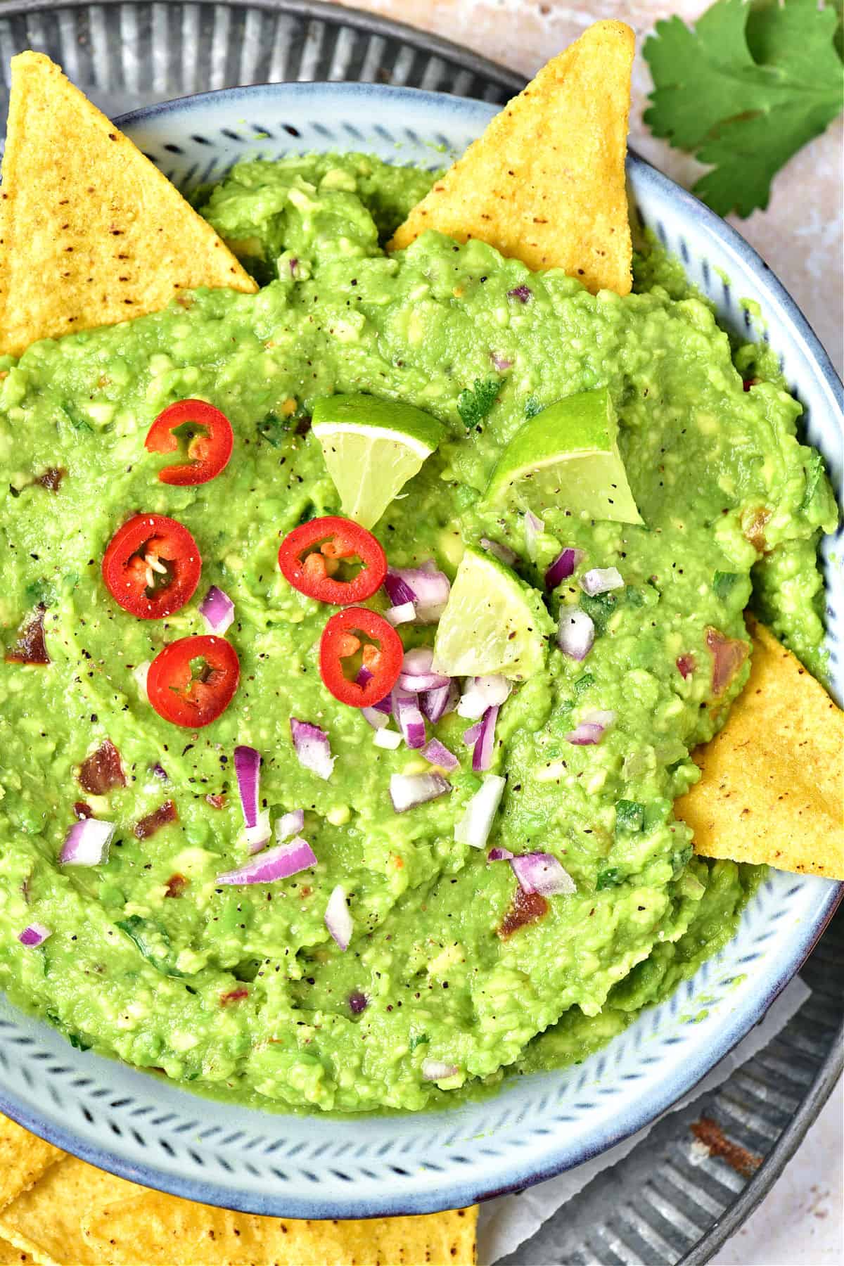 Red jalapeño guacamole in a blue bowl with tortilla chips and lime wedges.