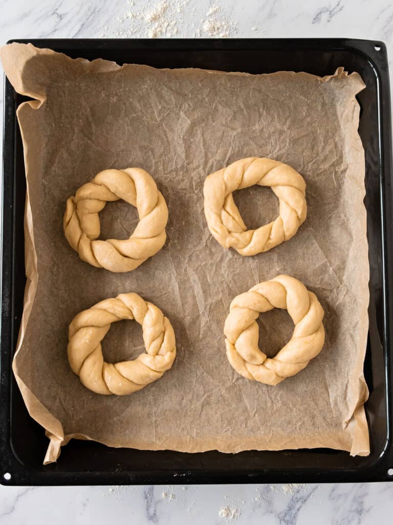 Four dough braids on beige paper on a black baking tray.
