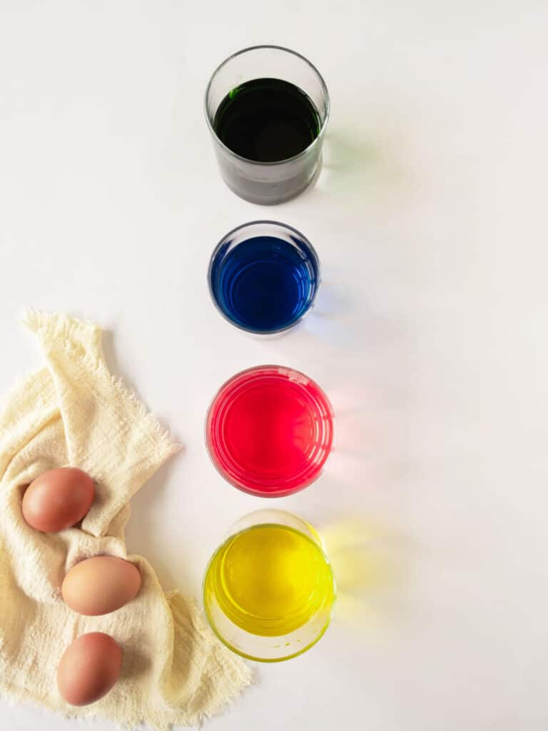 Four glasses with primary colored dyes. Brown eggs, white background.