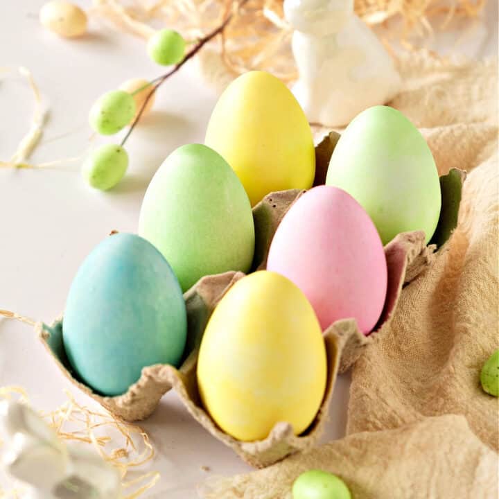 Pastel colored eggs in an egg cartoon. Beige cloth and a whitish background.