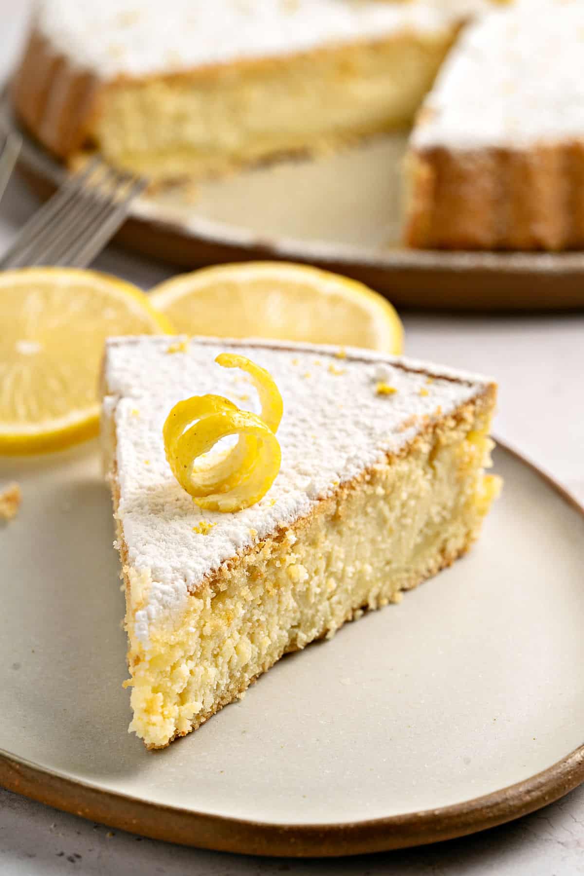 Slice of powdered sugar topped ricotta pie with double crust. Beige plate, pie in the background.
