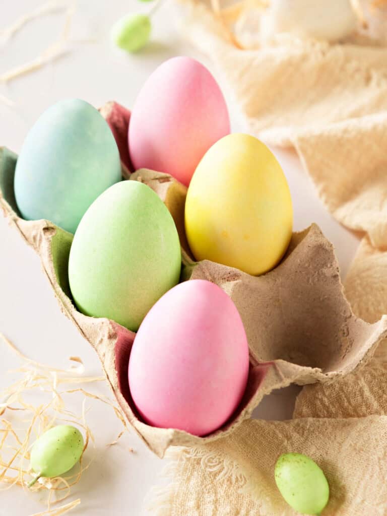 Beige egg cartoon with dyed Easter eggs. Beige cloth and white background.