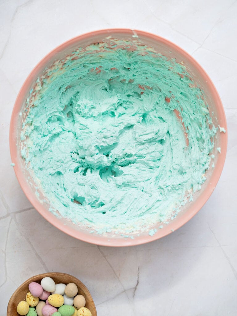Aqua buttercream in a pink bowl. Light gray background.