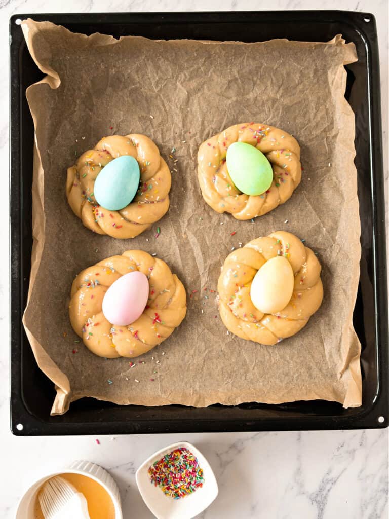 Black baking tray with beige paper and four braids with colored eggs.