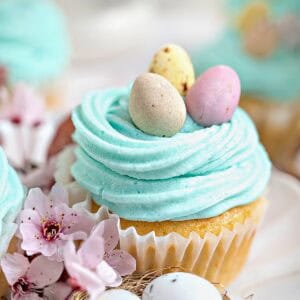 Close up cupcake with aqua buttercream mini eggs. Lilac flowers, white background.